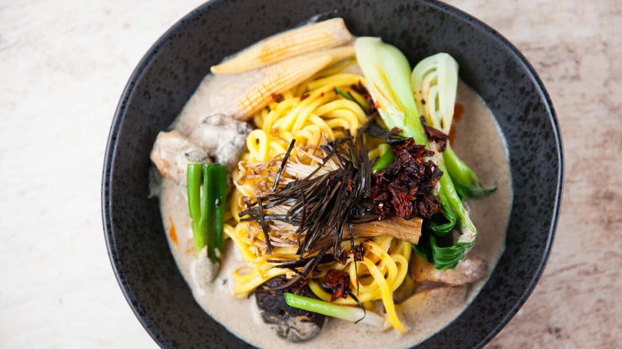 A black bowl holds a creamy noodle and bok choy soup.