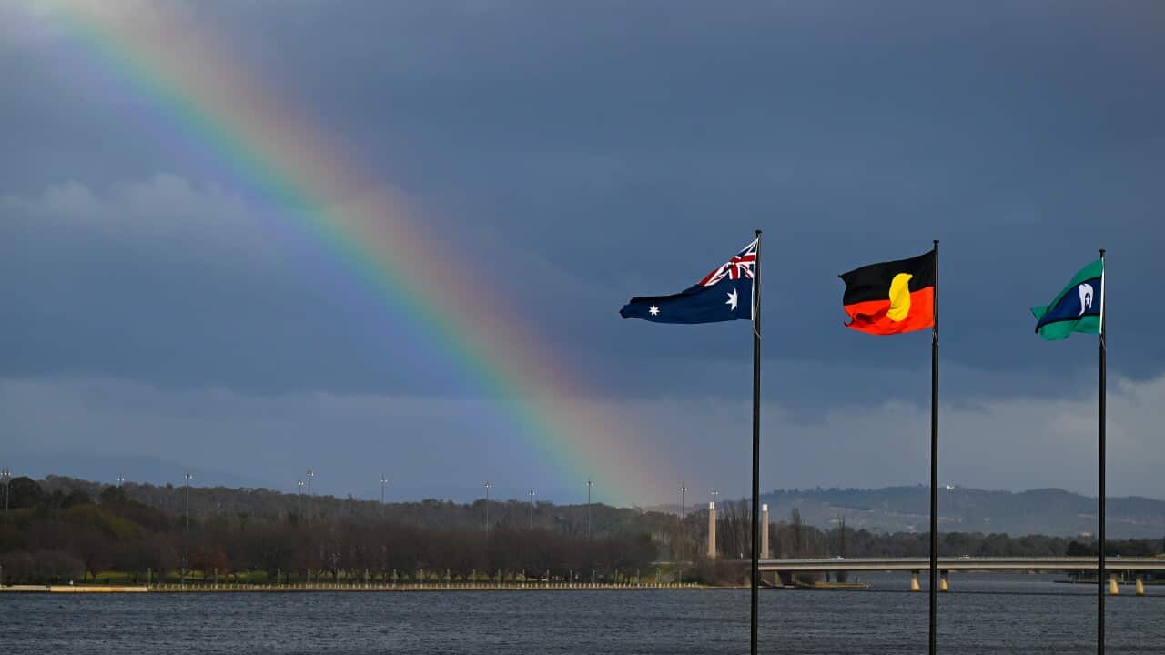 A rainbow is seen behind the Australian flag, the Indigenous flag and the flag of the Torres Strait Islands in Canberra.
