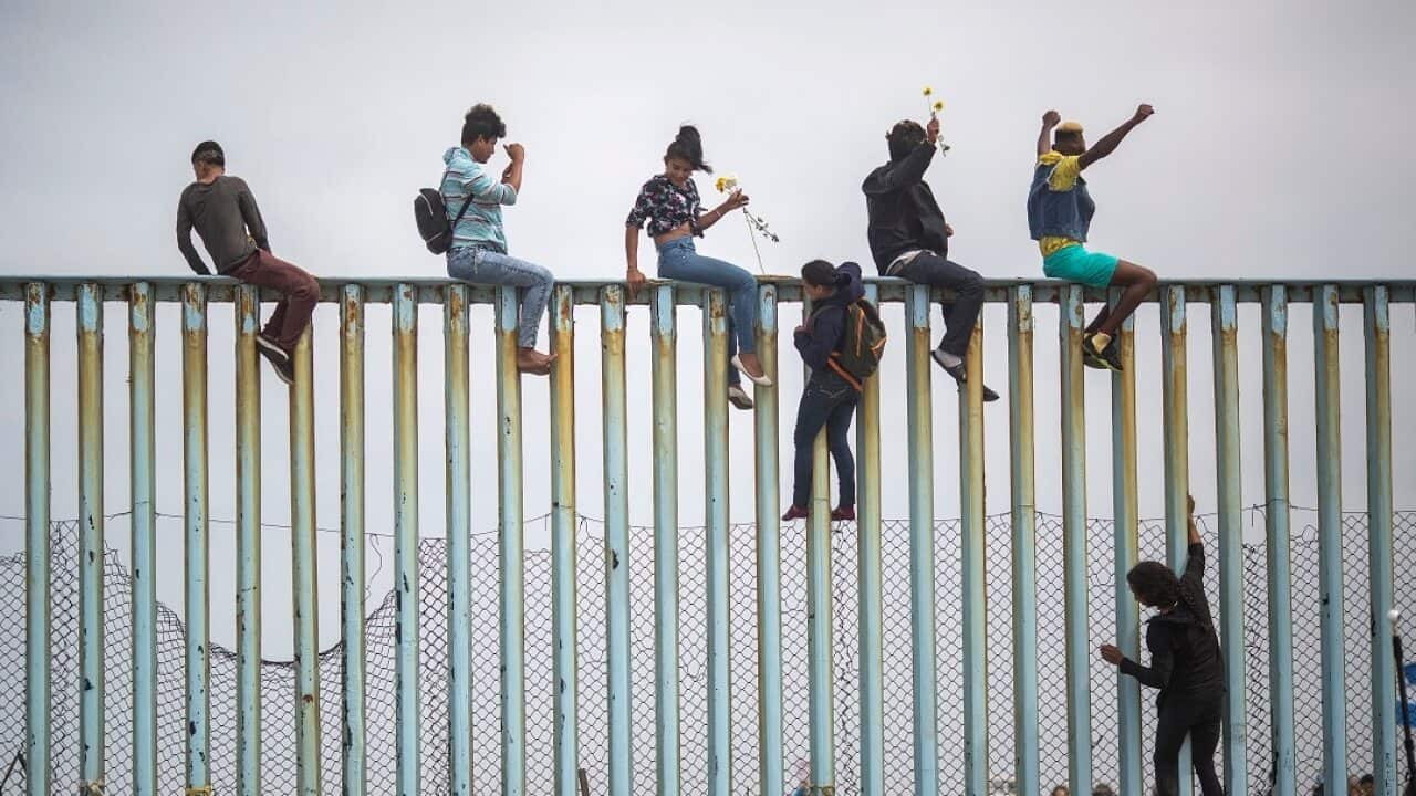 Members of a caravan of Central American asylum seekers scale a wall at the US-Mexico border.