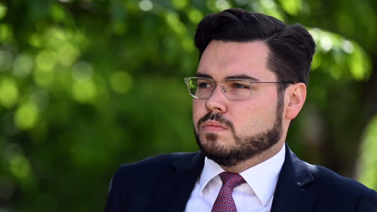 Man in suit and glasses walks outside.