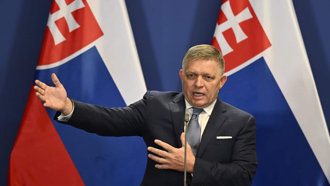 A man gestures at a podium in front of Slovakian flags.