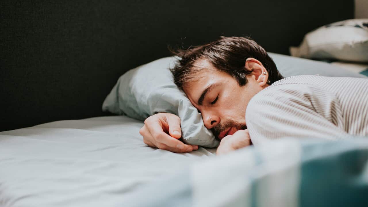 A man lies on his front, snuggled into a pillow, in an exhausted state
