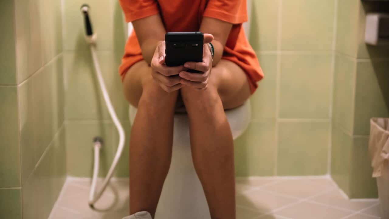 Woman sitting on a toilet holding a mobile phone in her hands
