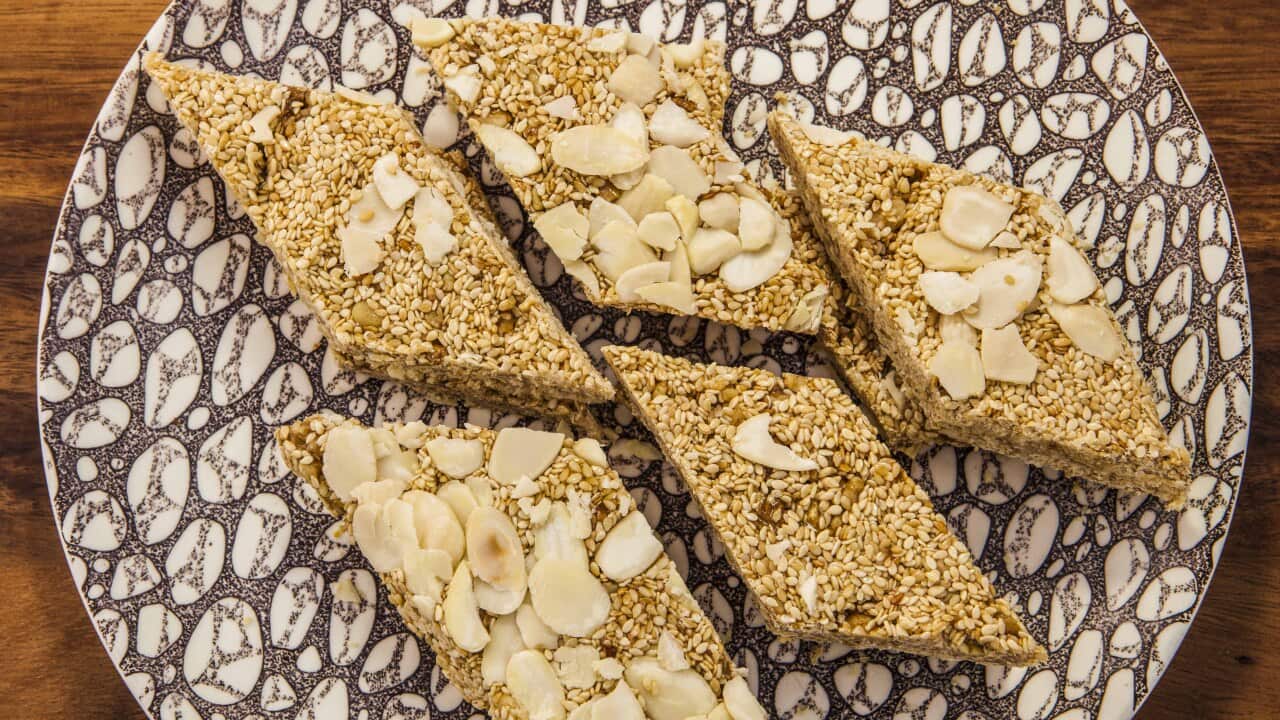 Five lozenge-shaped sesame bars sit on a patterned brown and white plate.