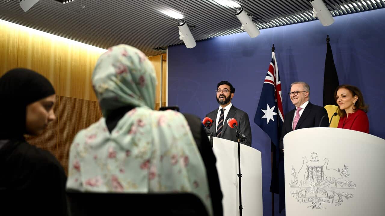 Three people delivering a press conference while two people wearing a hijab watch.