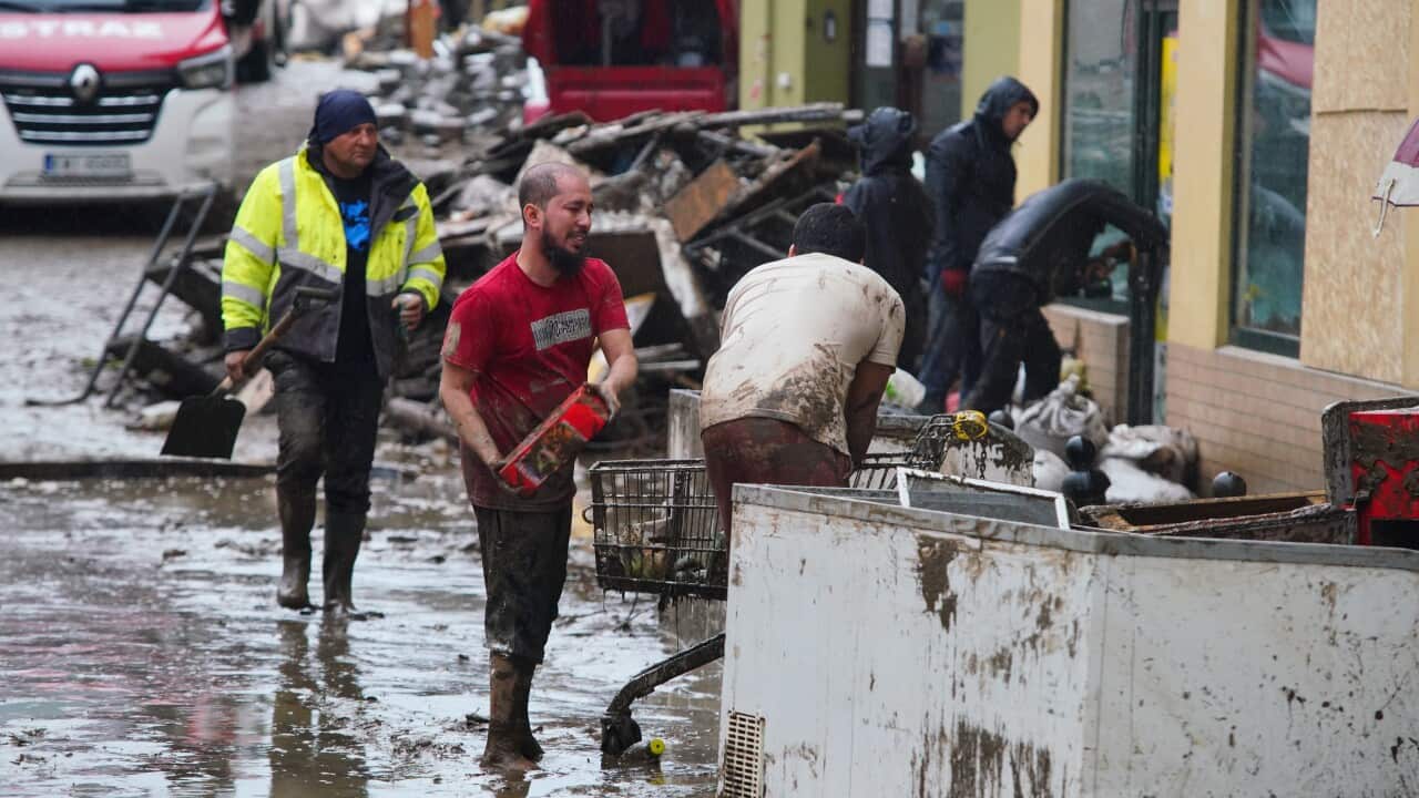 People walking in muddy street, two men carrying debris into shopping trolley.