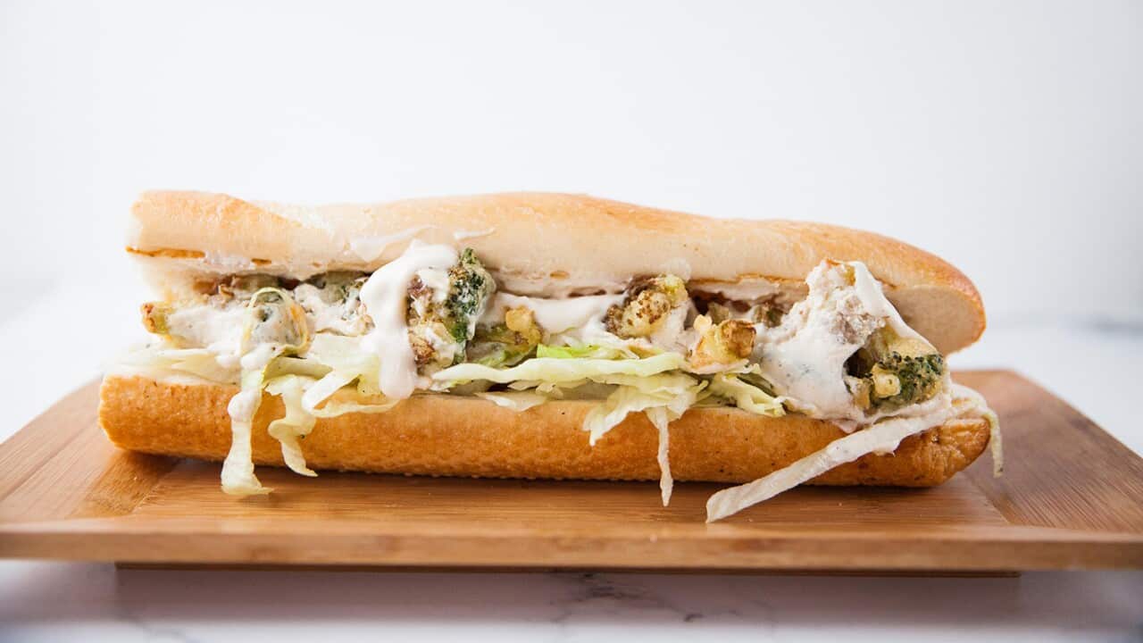 A bagutte section sits on a wooden platter. It is filled with cooked broccoli pieces and iceberg lettuce strands, with a creamy sauce.