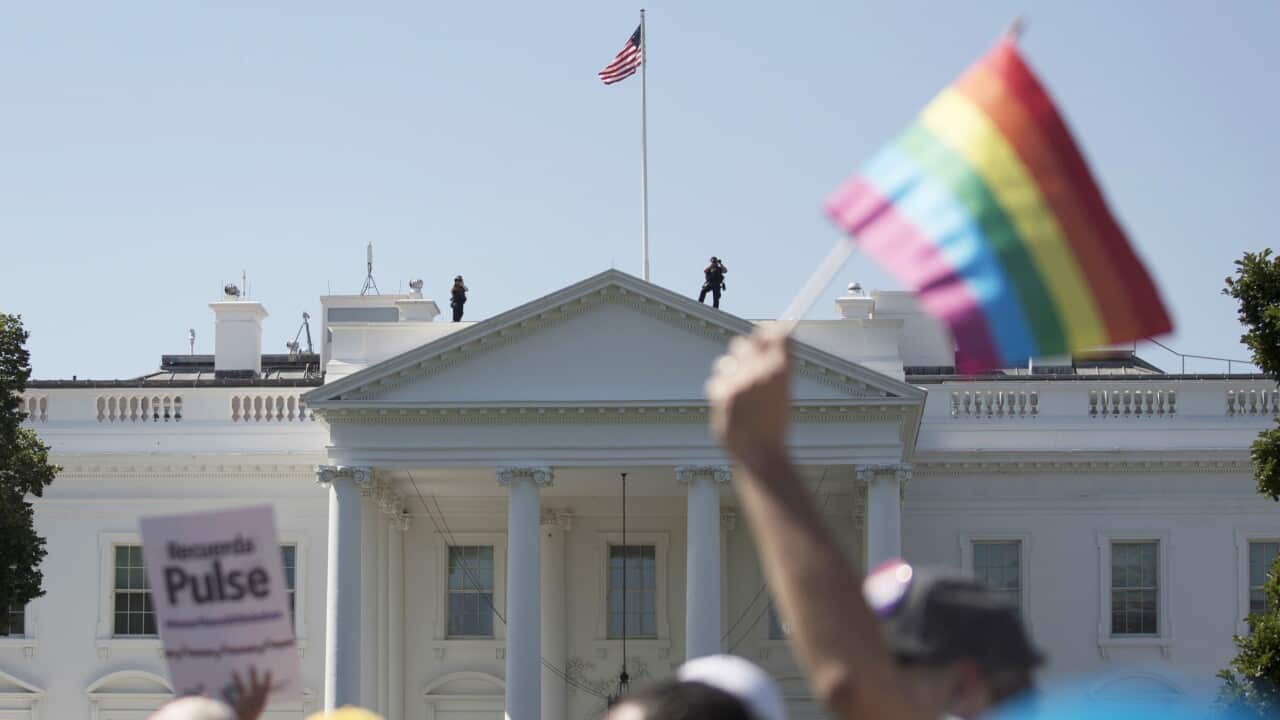 A protester waves a rainbow flag in front of the White House.