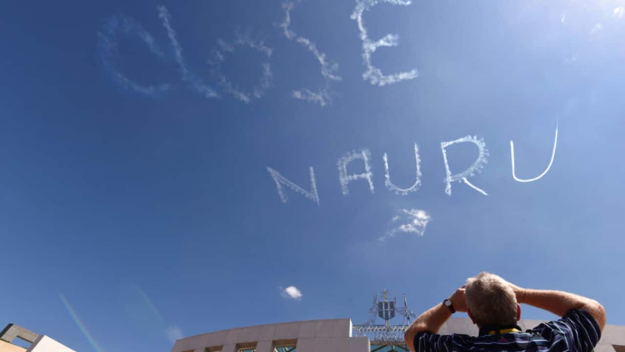  A man watches as a plane skywrites "CLOSE NAURU" above Parliament House in Canberra, Tuesday, Feb. 17, 2015. (AAP Image/Mick Tsikas) 