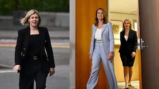 On the left, a woman with short blonde hair in a black suit. On the right, a woman in a lavender suit entering a room.