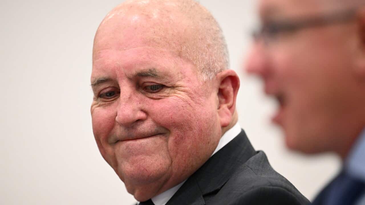 A man wearing a suit and tie looking on while another man speaks.