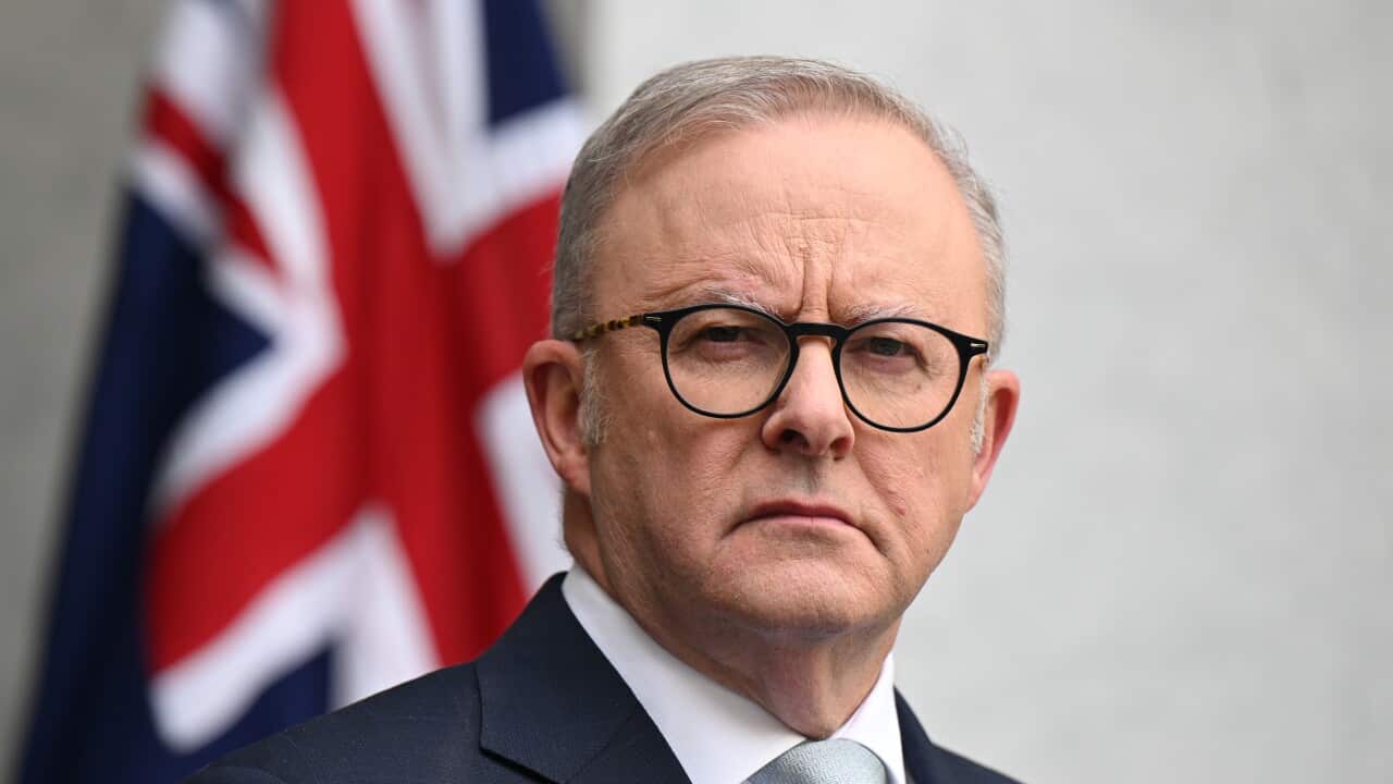 A man in a suit in front of an Australian flag