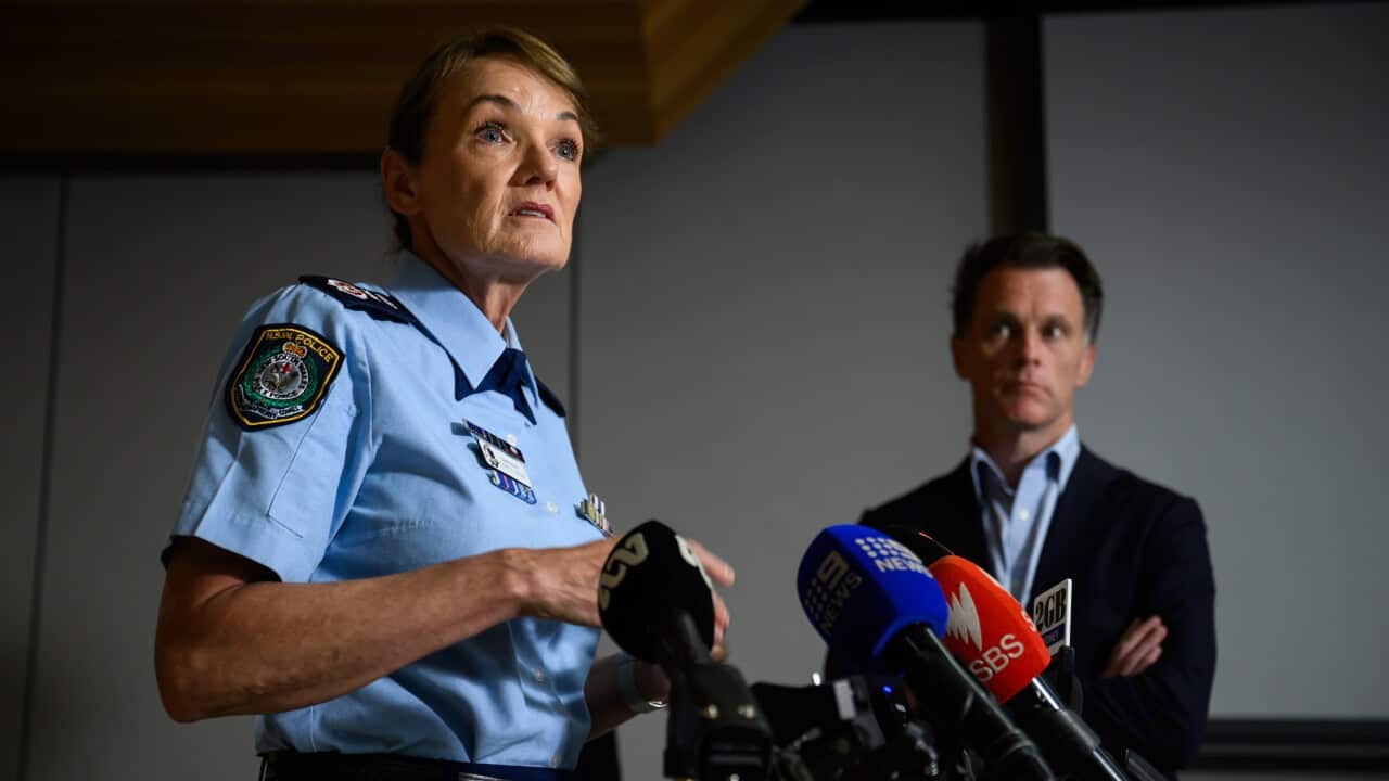 A woman in a police uniform speaks at a press conference while a man in a dark suit listens as he looks at her.