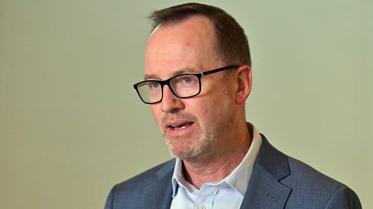 David Shoebridge wearing a blue blazer in front of a beige background.