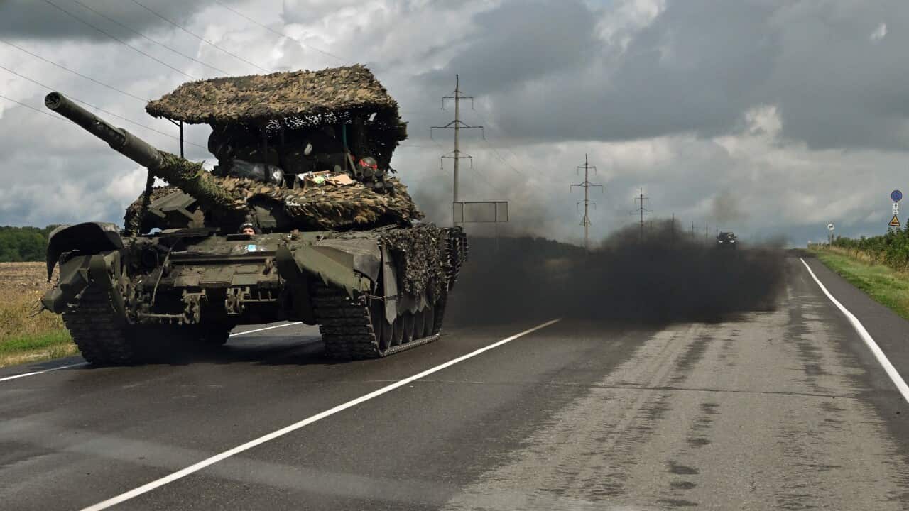 A tank drives down a highway followed by a large plume of black smoke