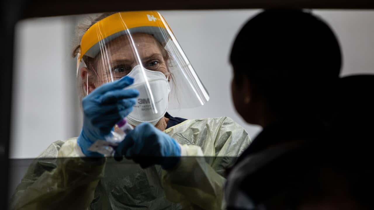 A woman wearing a personal protective equipment collects a COVID-19 test swab through a car window.
