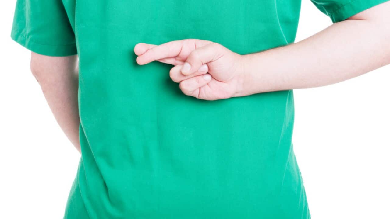 A man in doctor's scrubs crosses his fingers behind his back