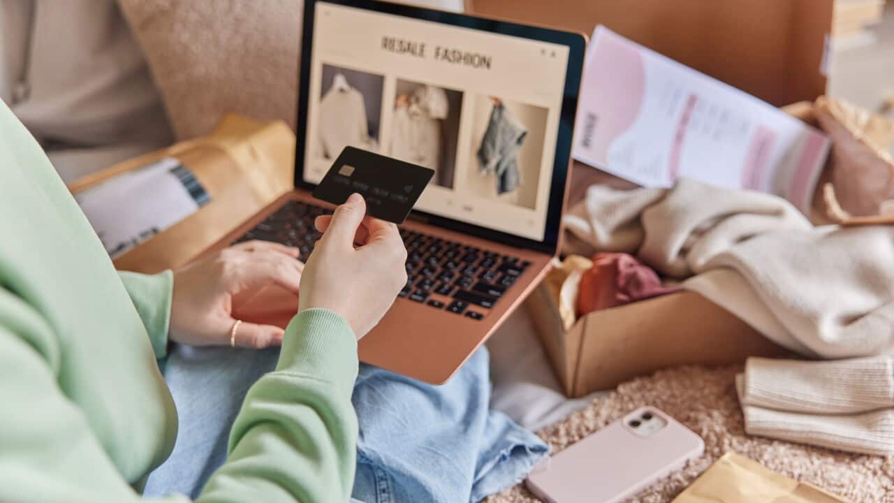 Cropped image of unrecognizable woman holds credit card and uses laptop computer makes shopping online buys clothes in internet webstore from home. Focus on banking card. Close up. Resale fashion