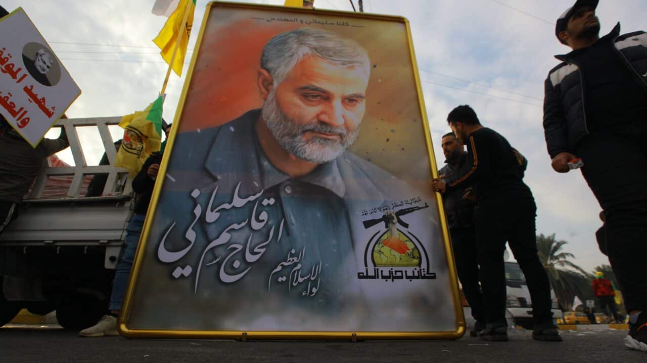 Mourners stand next to a giant portrait for Qassem Soleimani during a funeral procession.