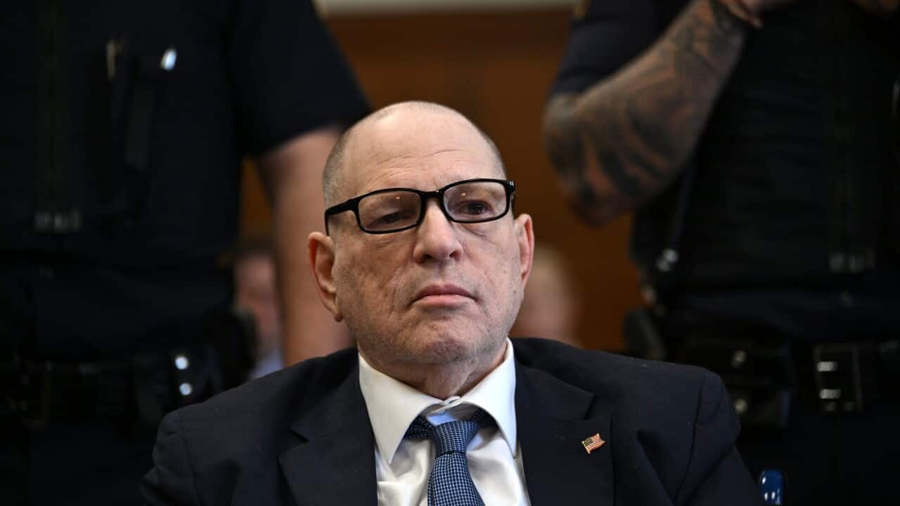A man wearing glasses, a dark suit and a blue tie is sitting.