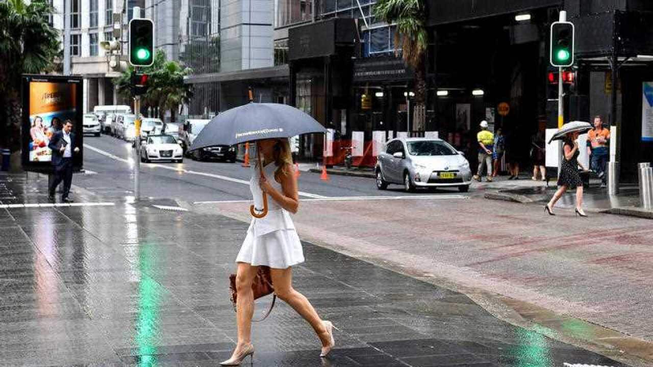 A woman in a short white dress,  holding a black umbrella, is crossing a road in the rain.