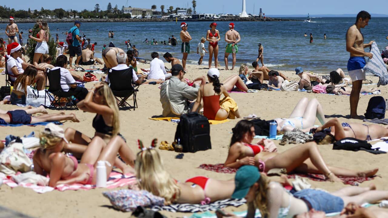People sitting and laying on the sand at a beach while others are in the water.