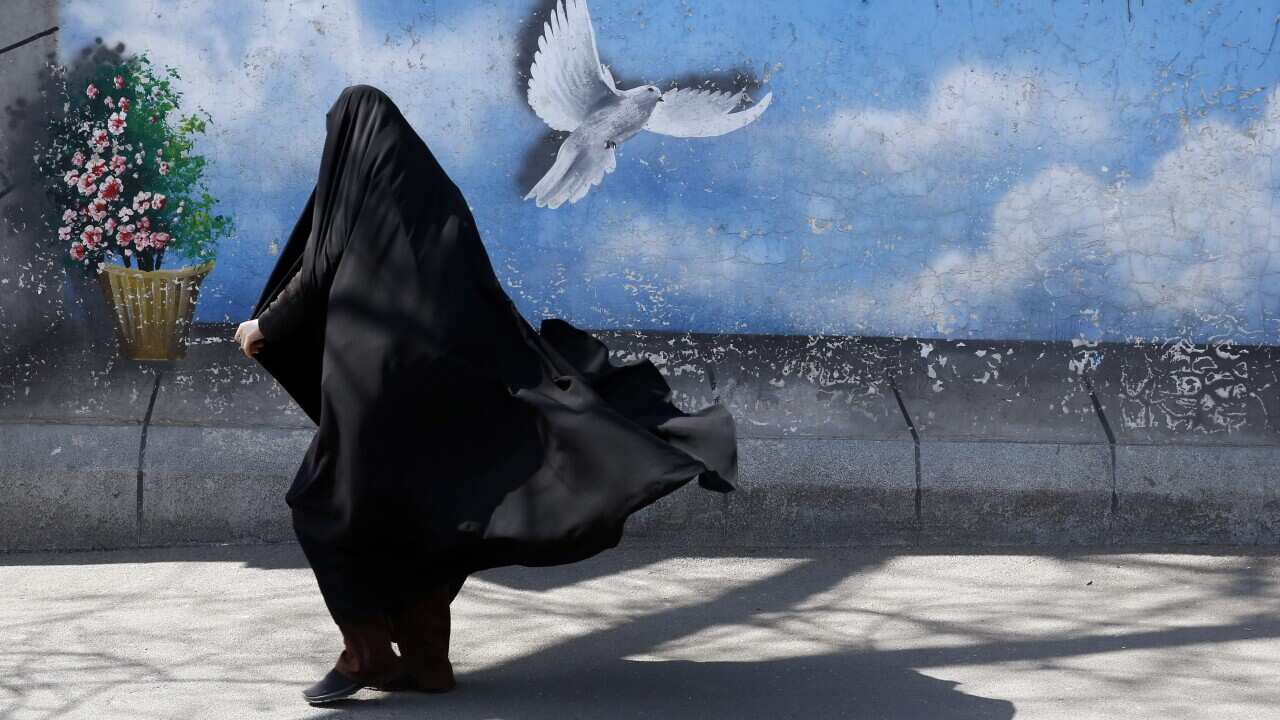 An Iranian woman walks past a wall painting of a peace bird at a street in downtown Tehran, Iran.