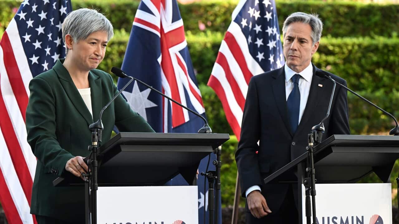 A man and a woman in suits stand at a podium with Australian and US flags behind them.