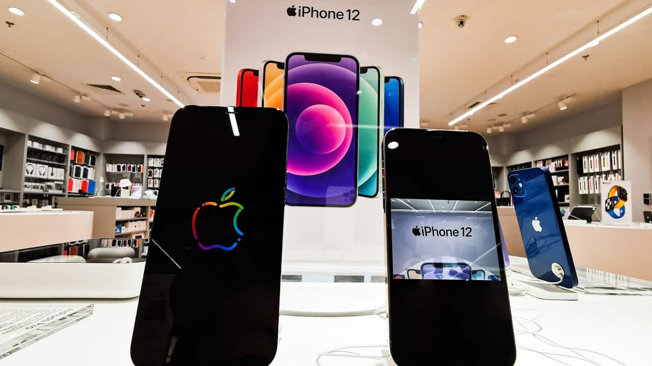 Two iPhones on display inside a store, with a large poster saying iPhone 12 in the background.
