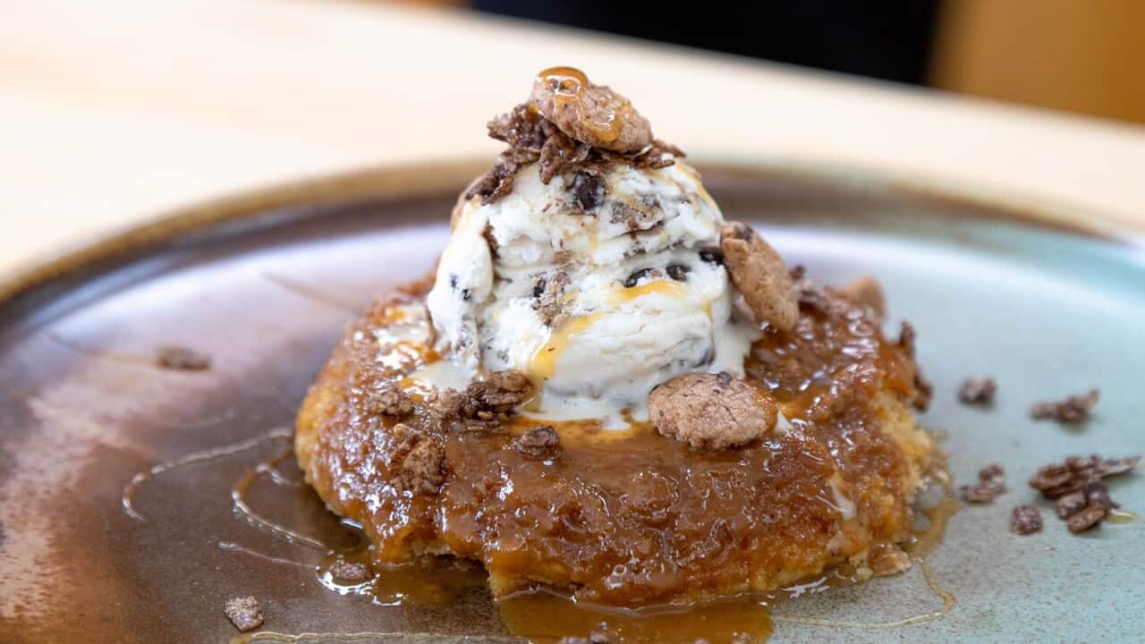 On a pottery plate, a low sticky cake oozing caramel sauce sits topped with a scoop of ice-cream.