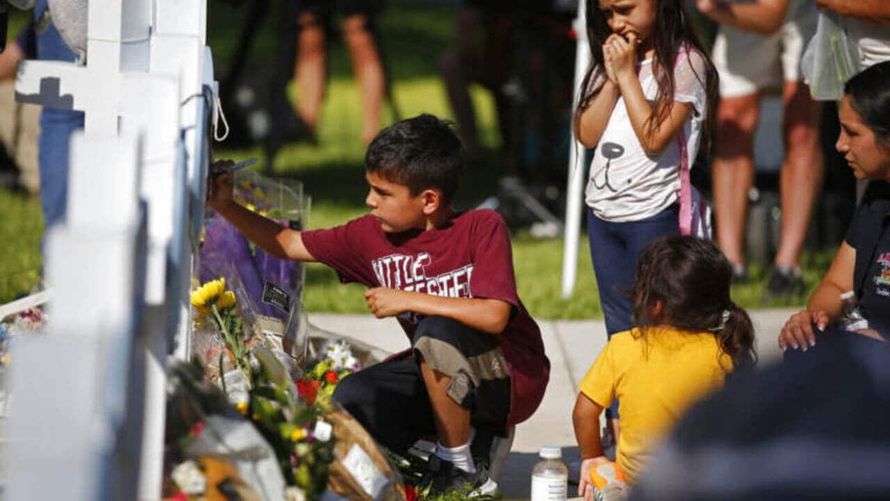 A child writes a message on a cross at a memorial site for the victims killed in elementary school shooting in Uvalde, Texas, May 26, 2022.