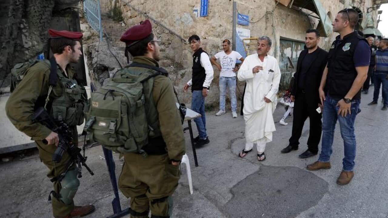 Palestinians ask permission to cross to a street in Hebron