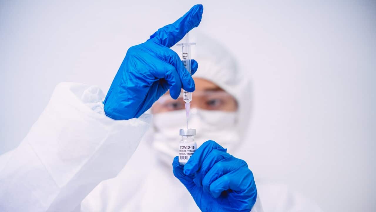 Doctor in protective gloves & workwear filling injection syringe with COVID-19 vaccine