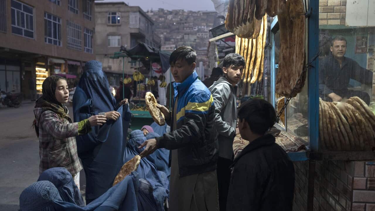 A man distributes bread to Burka-wearing Afghan women outside a bakery in Kabul