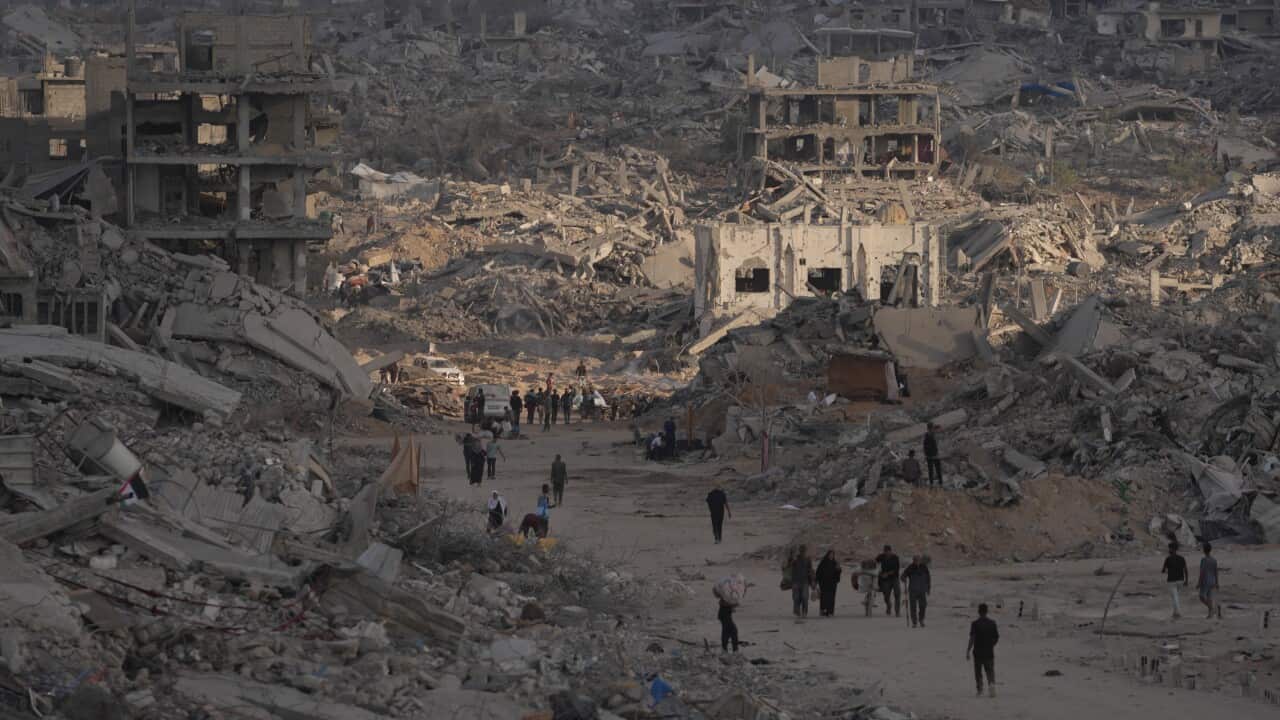 Palestinians walk among destroyed buildings in Gaza City, Sunday, Oct. 12, 2025