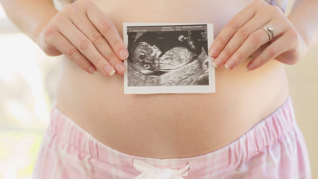 Caucasian woman holding sonogram over pregnant belly
