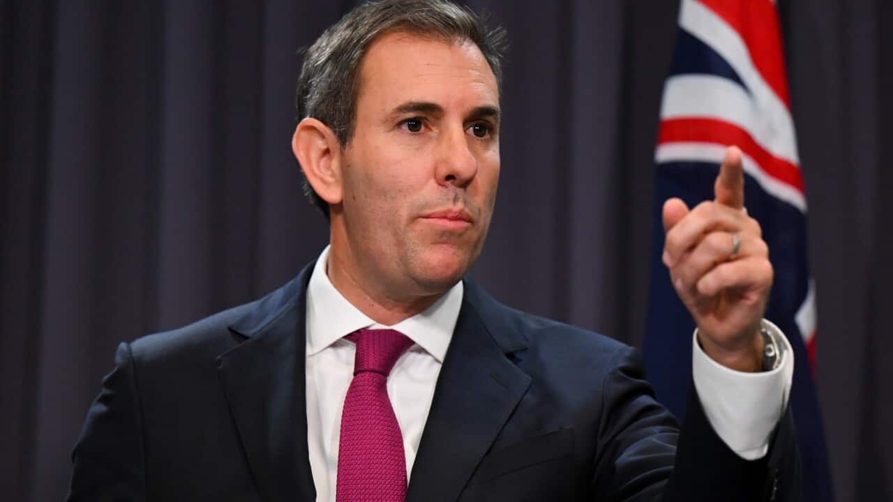A man in a suit and tie raises his left hand as he speaks at a presser.