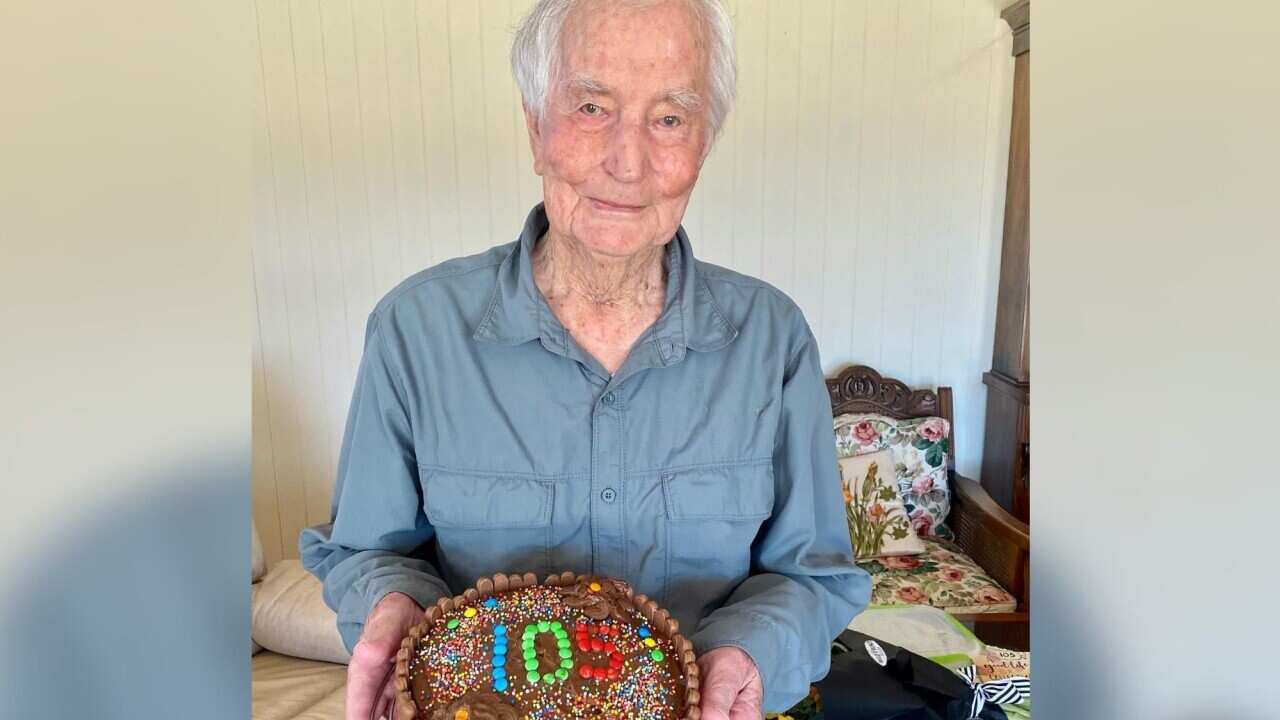 Colin Wagener holds a birthday cake with the number 105 on it.