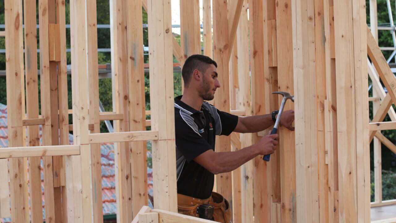 A labourer works on the timber frame of an unbuilt house