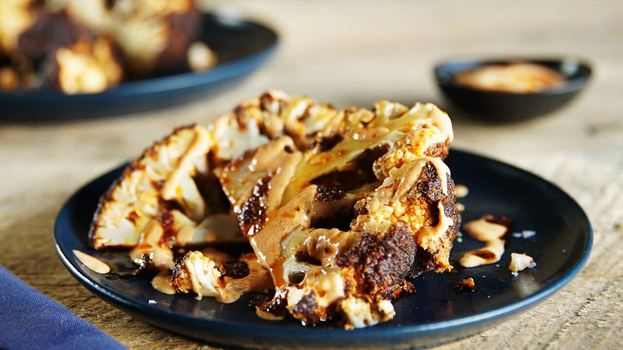 Cooked wedges of cauliflower, with brown edges, and drizzled with sauce, sit on a round dark blue plate.