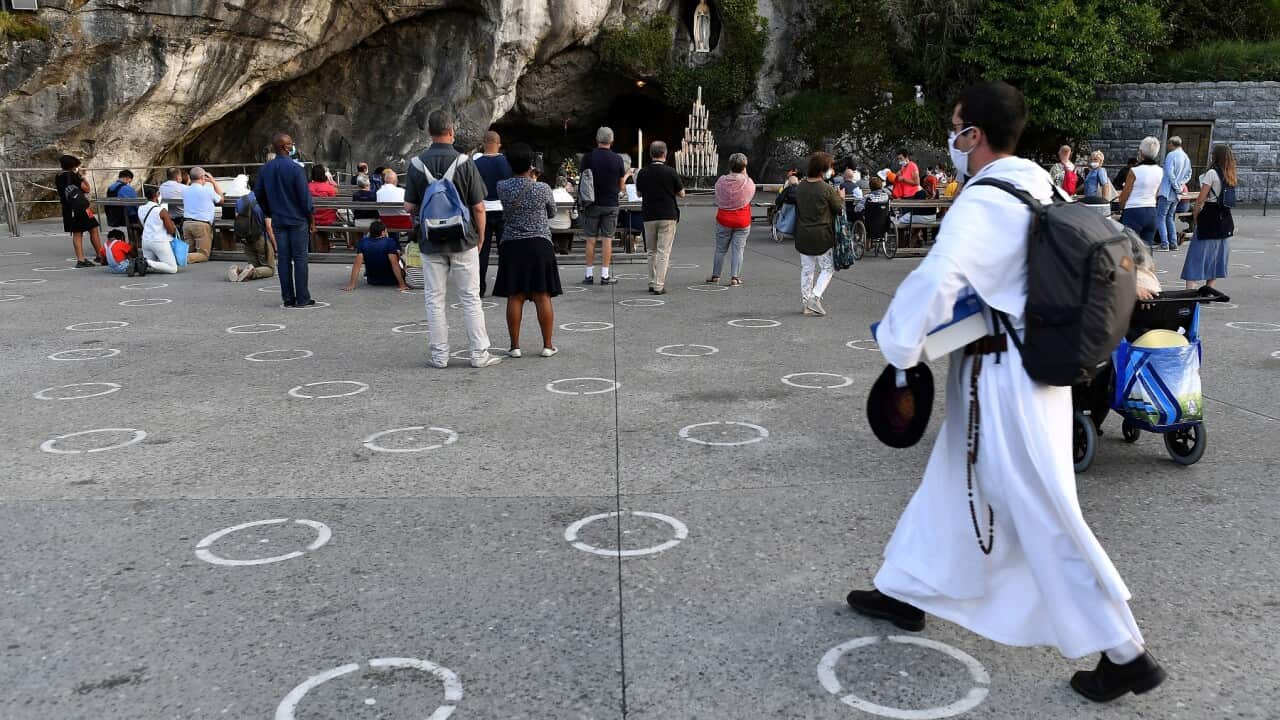 Faithfuls pray in front of the Grotte de Lourdes on designated areas painted on the ground.