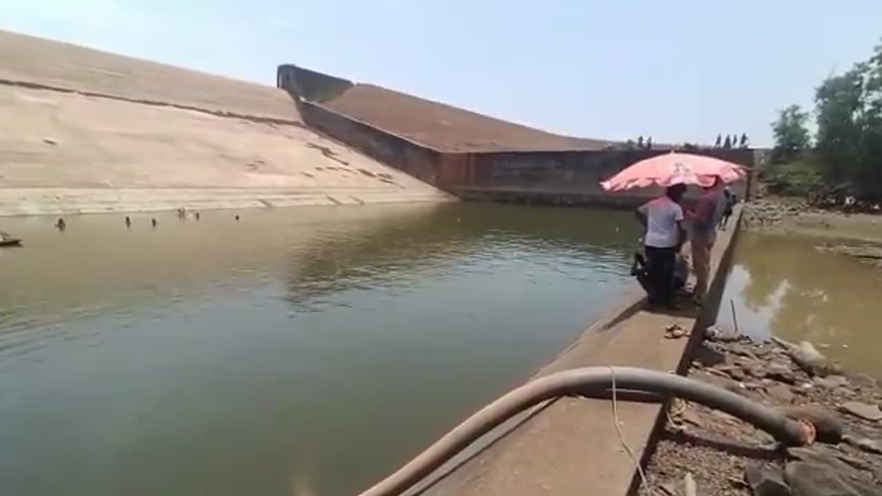 People wait under an umbrella as a pump drains a reservoir.
