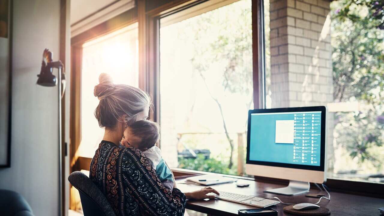 A young woman working at home while holding her newborn baby son