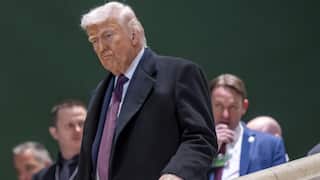 A man in a dark suit with a red tie and white hair walks down a set of stairs
