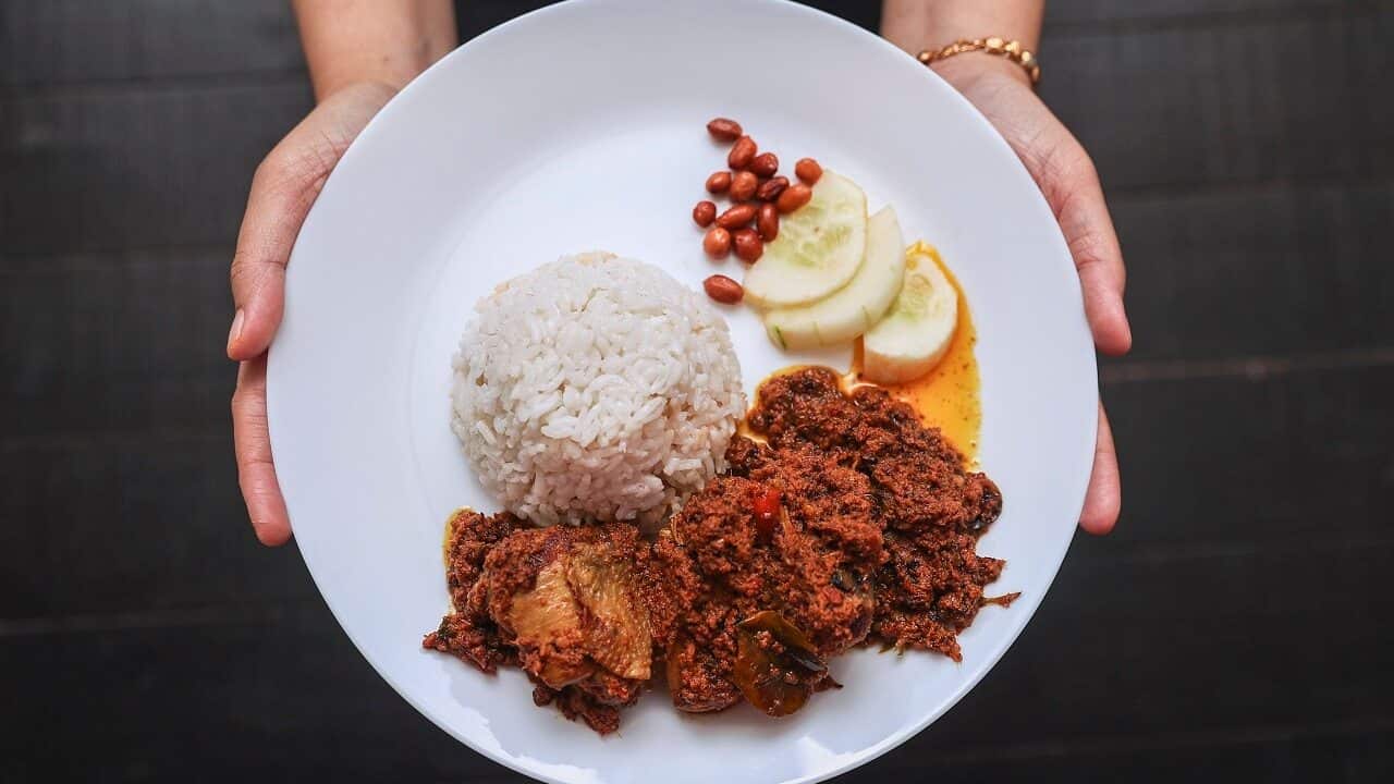 A women holds a plate with Malaysia's traditional dish 'chicken rendang'.