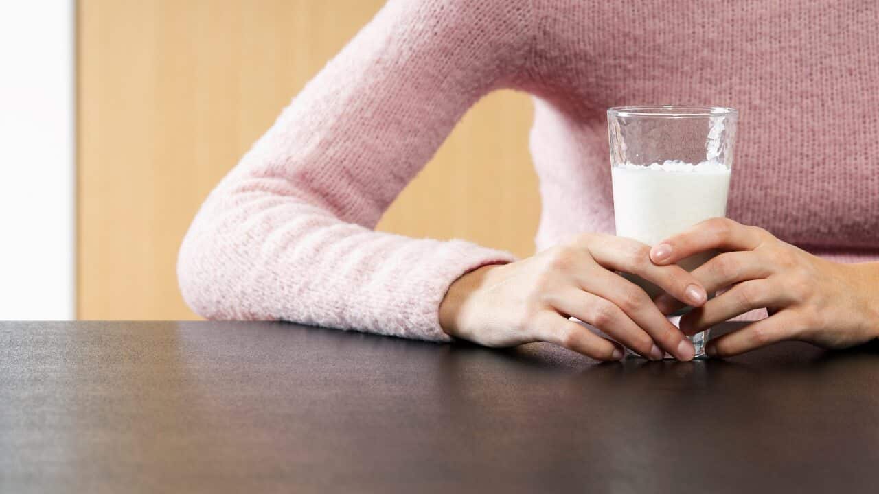 Woman holding glass of milk on table mid section