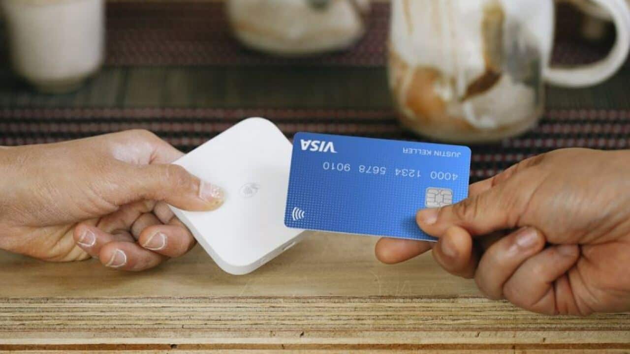 A person holding a Square payment reader while another holds up a Visa card