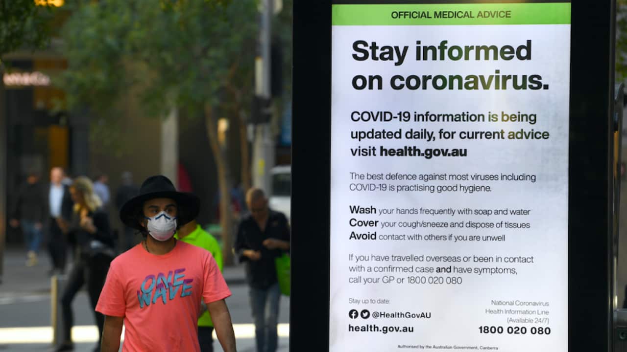 A man wearing a protective mask walks past official government medical advice in Pitt St, Sydney