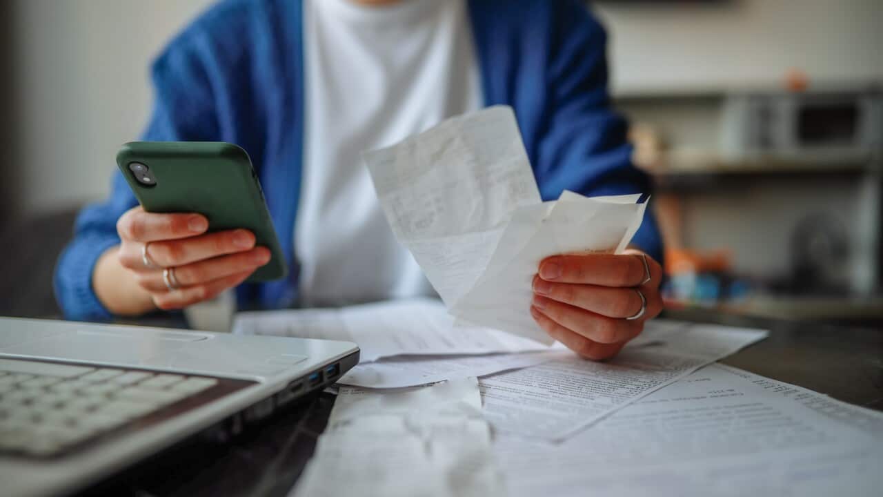 unrecognizable woman with a smartphone, laptop, and checks at a table at home.