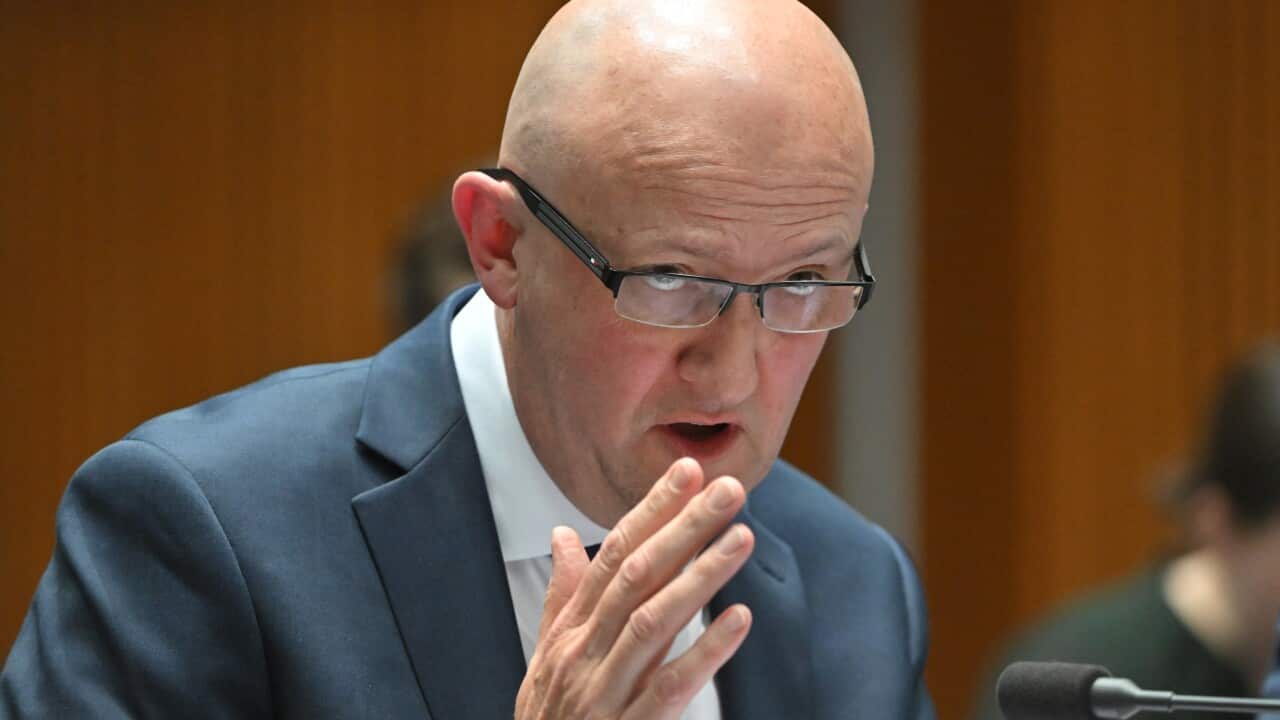 A man speaking at a desk into a microphone.